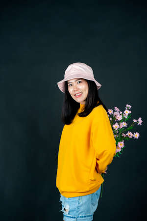 Portrait of an Asian woman in a clear yellow shirt holding flowers against a black background smiling happily in the studio looking at the camera.の写真素材