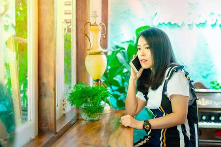 Portrait of a beautiful Asian woman using her mobile phone in a coffee shop, bakery.の写真素材