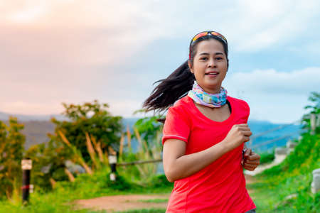 Half-body image of a female trail runner wearing a pink runner, sportswear, practicing on a dirt road on a high mountain with a happy mood, on a clear day Behind is a mountain view.の写真素材