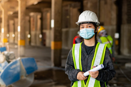 Young Asian female engineer wearing a medical mask to cover her mouth and wearing a white safety...