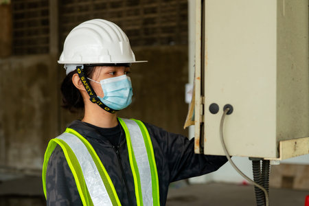 Young Asian female engineer wearing a medical mask to cover her mouth and wearing a white safety...