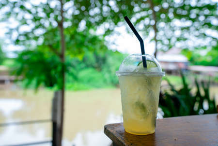 Lemon soda is placed in a plastic cup with a straw on a wooden table in a canal-side restaurant.の写真素材