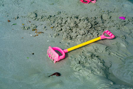 Children's toy shovel pink and yellow for playing in the sand. laying on the sand by the seaの写真素材