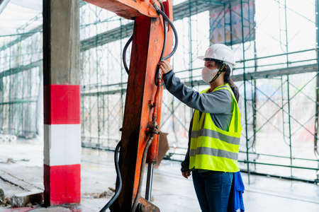 PORTRAIT, an Asian female engineer Wear a reflective vest and a white safety hat. Checking the machines at work construction site areaの写真素材