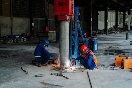 A construction worker in safety gear is using gas. weld the steel of the pole to be joined as one...