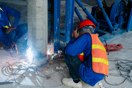 A construction worker in safety gear is using gas. weld the steel of the pole to be joined as one...