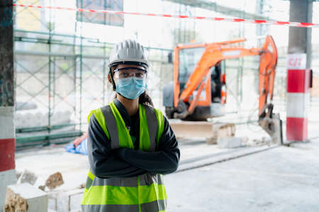 Portrait of an Asian female engineer Put on a brightly colored shirt. and wear a white safety cap standing with his arms crossed at the construction siteの写真素材