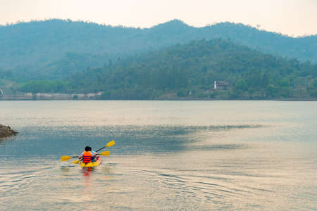 A large reservoir in the morning, behind a high mountain with tourists canoeing in the water.の写真素材