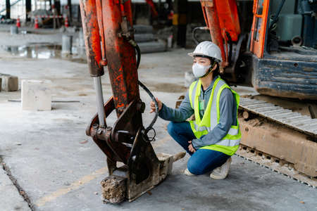 PORTRAIT, an Asian female engineer Wear a reflective vest and a white safety hat. Checking the machines at work construction site areaの写真素材