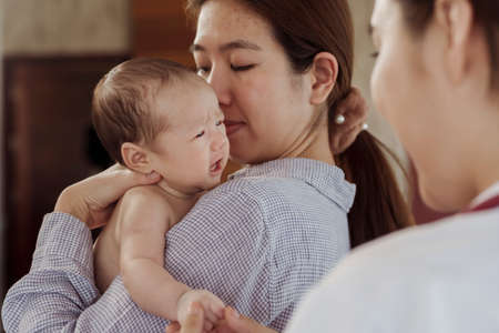 A newborn baby is crying on her mother's shoulder for fear of the doctor coming to check because she is sick in the hospital.の写真素材