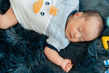 Close Up Newborn, 2 months old, Asian is sleeping on a black-grey carpet with her mother's hand on her chest to make the baby sleep well.の写真素材