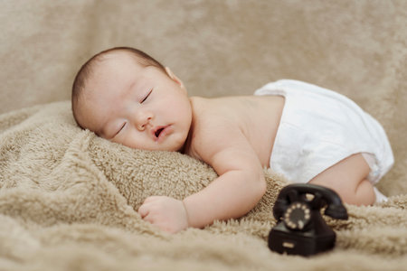 close-up photo of face of an Asian newborn sleeping happily on a brown carpet.