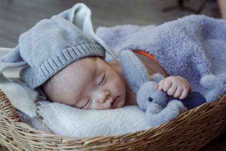 Cute Asian newborn baby. wearing a blue rabbit Sleep well. By hugging the rabbit doll. lying in a wicker basketの写真素材