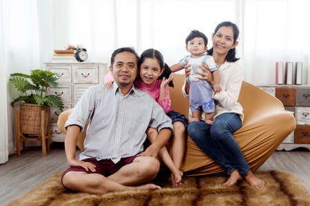 Love and warmth in Asian families, parents and children. Sitting on the sofas in the living room, with love and warmth from parents to the newborn baby and sister.の写真素材