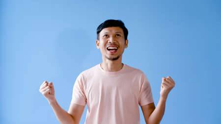 Asian man with mustache showing great joy. With both hands at your sides, body language. Isolated indoor studio on blue background.の写真素材