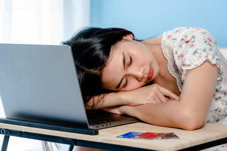 adorable Asian woman falling asleep on the arm on table in front of a laptop computer after a tiring...