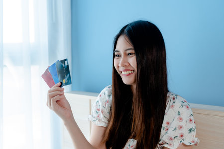 A beautiful Asian girl,sitting on the bed, wearing a white floral shirt, is ordering online through...