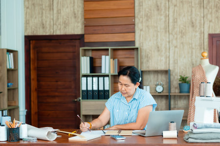 Asian senior woman designing clothes to sell in her own shop in office, Professional small business owner in clothing design, Concept online store.の写真素材