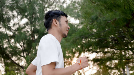 Good-looking Asian man wearing white t-shirt, jogging by the sea in the evening, happy expression, popular tourist destinationの写真素材