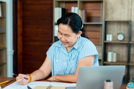 Asian senior woman designing clothes to sell in her own shop in office, Professional small business owner in clothing design, Concept online store.の写真素材