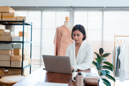 The clothing store owner was talking on the phone to take orders, while writing down details on his laptop computer,Professional small business owner partner in clothing design.の写真素材