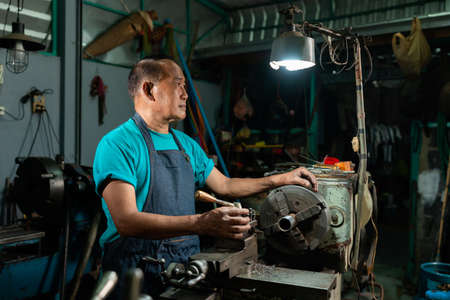 Portrait of Asian senior man working as a steel lathe is preparing work and equipment to turn steel and a small lathe in the family industry.の写真素材