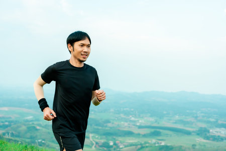 Portrait of half-body portrait of Asian male runner in black training on a high mountain. The back view is high mountain, with beautiful scenery. In the evening the air is fresh and atmosphere is good.の写真素材