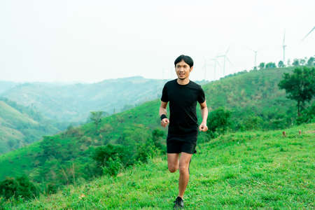 Portrait of an Asian male trail runner running. On the high mountains, beautiful scenery. It's trail running training. on a bright day Behind is a beautiful mountain view.の写真素材
