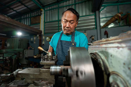 Portrait of Senior Asian man is a mechanic who owns a family business lathe. A small industrial lathe is being installed and initialized..の写真素材