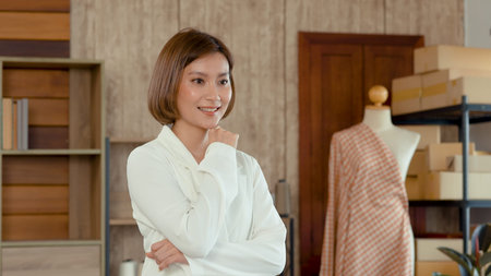 Young woman Asian Tailor Shop Owner, Close-up of the face of female mechanic who poses with her arms crossed behind her desk, Small business Professional Design clothes to sell online.の写真素材