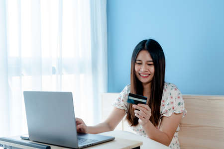 close-up beautiful Asian girl takes a blue credit card to fill out card information Sit online shopping through a laptop computer, to use a credit card to pay online. happy faceの写真素材