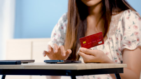 Close-up of a beautiful Asian girl's hand red credit card to fill out card information Sit and shop online via mobile phone, to pay online via mobile phone.の写真素材