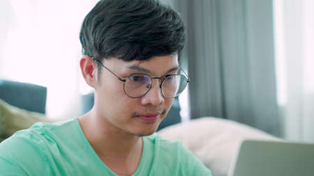 Close-up of a young Asian man wearing a green shirt, with a serious expression on his work, inside the house.の写真素材