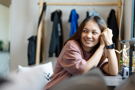 A cute young Asian woman sitting on her bedroom desk smiling happily.の写真素材