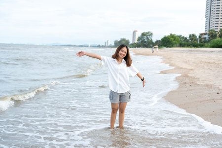 A young tourist, a long-haired Asian woman in a white shirt, is strolling along the beach where the...