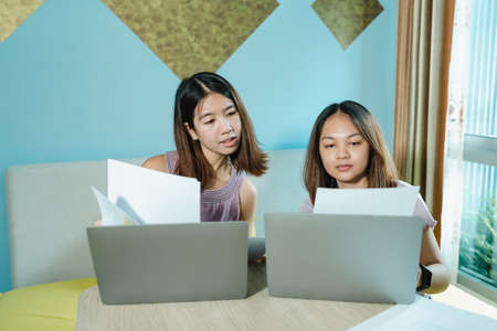 female tourist Asian couple relaxing in hotel But had to work on vacation. 2 women working in bed with computers in the room under stress. help each other urgently to deliver the work to be completedの写真素材