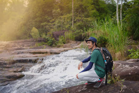 Asian young man, tall and slender, Wear your favorite blue hat, Sitting chilling on a large rock, enjoying the cool breeze, He looked happy with the nature in front of him.の写真素材