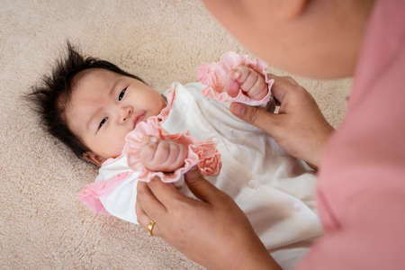 Asian single dad is caring for his 3 month old baby in bed and playfully teases each other to delight his little daughter. A newborn baby lies in bed with his father watching over him.の写真素材