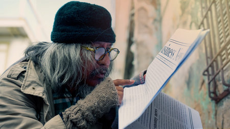 An old Asian man in glasses and a black hat, dressed in a dirty, homeless man, is reading the...