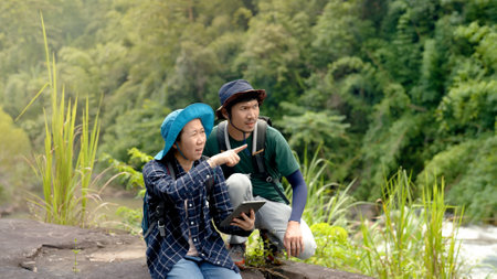 Asian man and woman couple are exploring routes and maps from their tablet to prepare a path to walk in the forest to their destination for a weekend getaway after a hard day at work.の写真素材