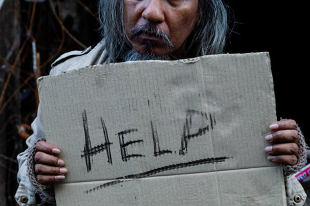 Close Up A sign for help in the hands of a dirty, dressed old man who is homeless, with food and work to do with no money to buy and sleeps on the streets every night. Homeless do not have homeの写真素材