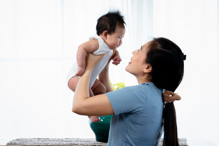 Asian single mom, holding up his daughter, teasing his daughter by holding it up and down, slowly, And Khun Mother put her sweet nose on her daughter's cheek gently, He teases and plays with baby.の写真素材
