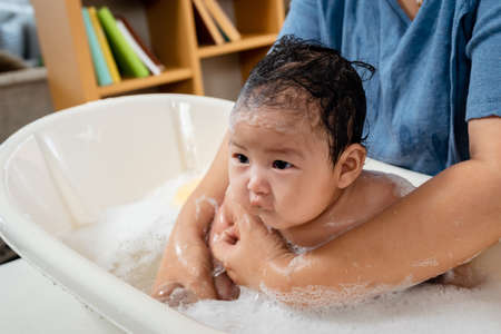 Asian baby girl, taking a bath, he bathes in a bubble bath, with a single mother bathing her daughter, gently, The daughter's face and body were filled with bubbles.の写真素材