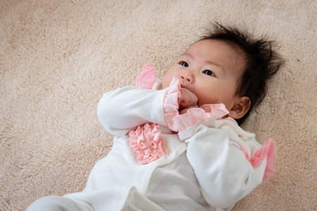 Asian newborn baby girl 3 months old is lying on the bed with her hands clasped and releasing and covering her face happily while waiting for her mother to take care of her.の写真素材