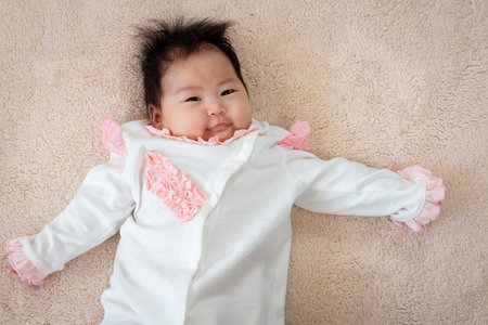 Close-up of a 3-month-old Asian baby lying in bed with both hands comfortably spread out. and her...
