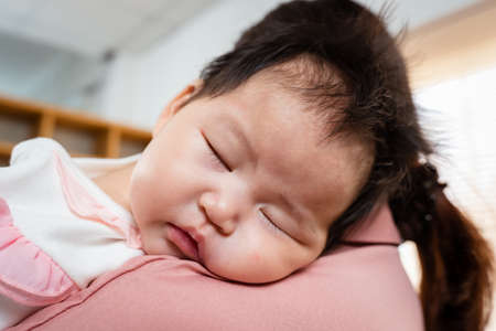 Close Up is a 3-month-old newborn Asian girl who her mother is holding. A single mother is holding her newborn baby by soothing her to sleep. in the bedroom of the house. Family and Healthy.の写真素材