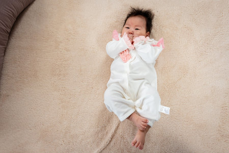 Close-up photo of a 3-month-old Asian baby lying in bed with both hands comfortable to her mouth....