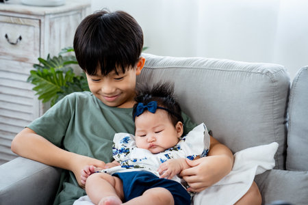 boy sitting on the sofa,in the living room of the house, He held two newborn girls in his embrace, and let him sit on his lap, He talked to his sister, and held her hand tenderly.の写真素材