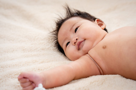 newborn baby face close-up, lying on the brown bed, The little boy's eyes were staring at something, anxiously, black eyed little boy, The child slept without clothes because of the hot weather.の写真素材