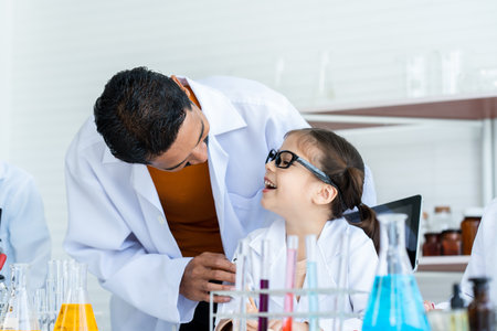 A male teacher in white lab coat ask a little Asian girl how about doing experiment. A girl with glasses explain how to process experiment step by step. They both smile together while checking data.の写真素材